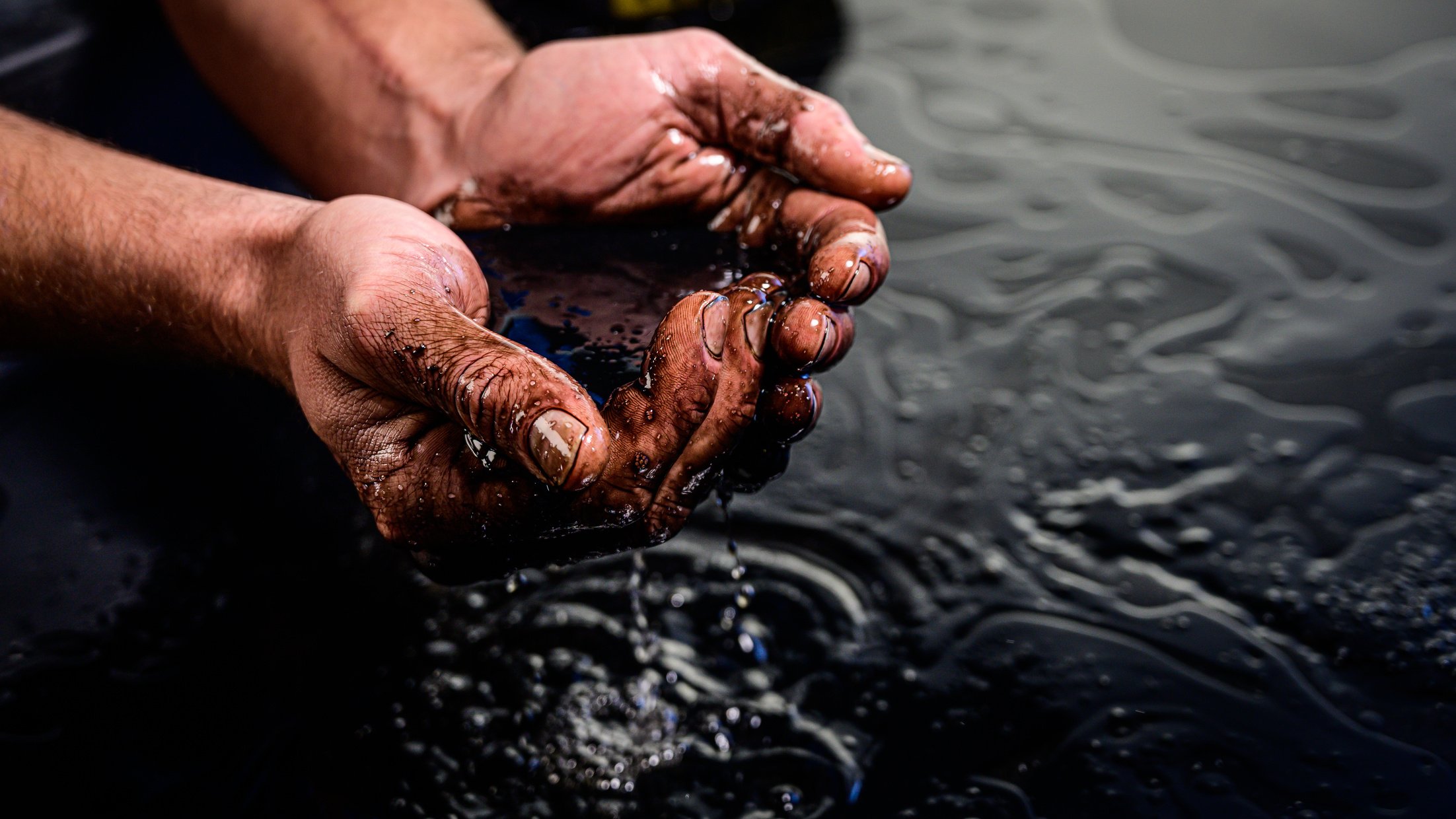 Hands cupping crude oil spills in water